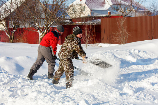 Two men are shoveling snow in front of a house