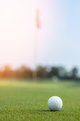 Golf ball on green course, grass lawn with blur hole pole flag background with  greenery field and blue sky copy space for golf sport tournament backdrop