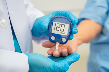 Asian doctor using digital glucose meter for check sample blood sugar level to treatment diabetes.