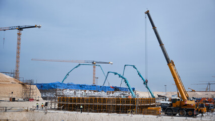 Jibs of concrete pump trucks make concrete conveying at construction site. Arms of concrete pumps and cranes during concrete pouring works. Cement casting at construction site