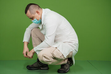 A Medical Professional Tying Shoelaces While Squatting in a Green Background