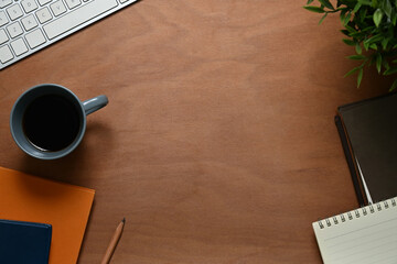 Wooden desk with cup of coffee, notepad and computer keyboard. Top view, Flat lay