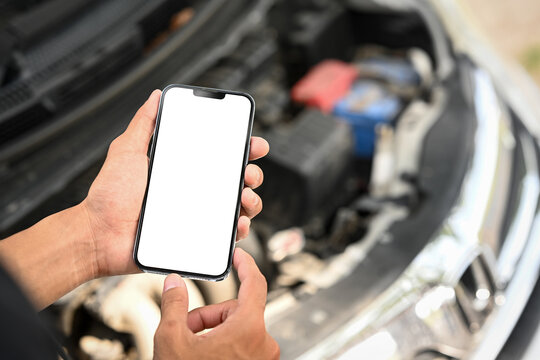 Man using smartphone near an open car hood while inspecting the car engine