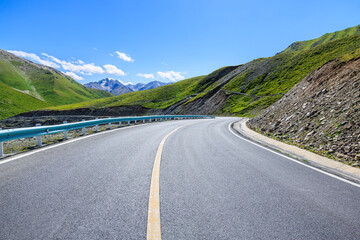 Fototapeta premium Countryside asphalt road and green meadow with mountain nature landscape on a sunny day. Road trip.