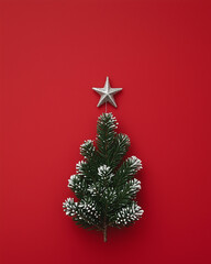 A Christmas tree made of small green branches with snow on it with a star on top on a red background. Minimal winter and Christmas card with copy space