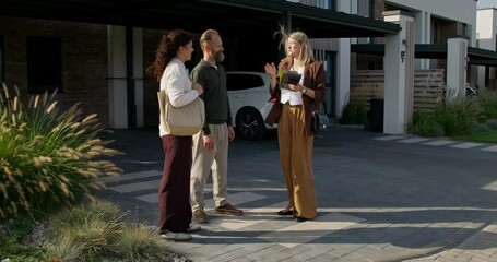 The realtor shows the booklet to customers standing near the townhouse for sale