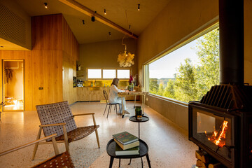 Woman enjoying breakfast at a wooden table, with a view of lush greenery through a large window. Fireplace crackling warmly, creating a serene atmosphere