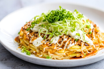 Japanese okonomiyaki topped with cabbage and mayonnaise swirls, presented on a minimalist plate, softly blurred background