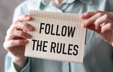 Hands holding a sign with the words Follow the Rules on a blue background