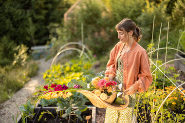 A young woman holding a basket of freshly picked flowers in a blooming garden at sunset. A perfect...