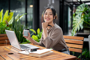 An Asian woman working remotely from a serene cafe, sitting at an outdoor table with her laptop.