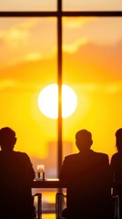Obraz premium Silhouettes of people sitting at the table in front of large windows with orange light, sunset outside. Group business meeting concept.