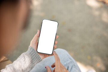 A close-up of a woman sitting outdoors in a park, using her smartphone, touching the screen.