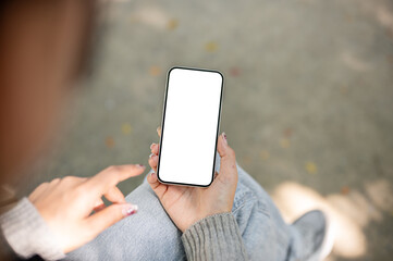 A close-up of a woman sitting outdoors in a park, using her smartphone, touching the screen.