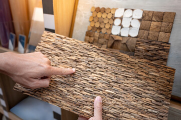 Coconut shell pattern design concept. Designer hand pointing at sample of coconut shell board with mosaic tiles on display shelf in material showroom. Natural finishing for tropical style