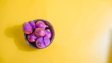 red onion in wooden bowl on yellow background 