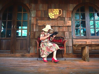 Fototapeta premium Beautiful young woman in a hat and dress is sitting on the porch of a wooden house.