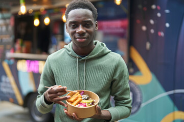 Portrait Of Teenage Boy Eating Vegan Mezze Bowl At Outdoor Street Food Market