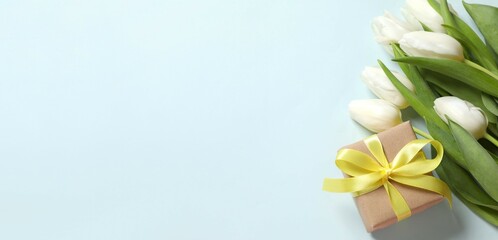 Beautiful fresh tulips with a gift box on color background