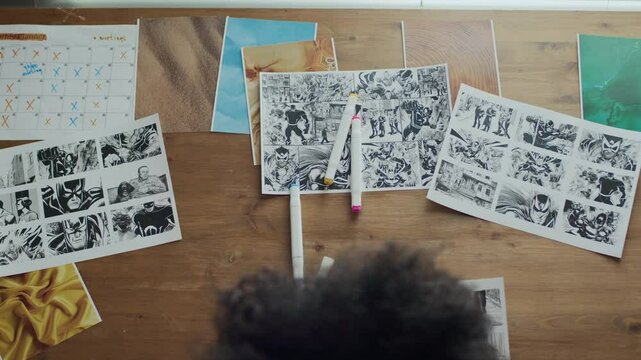 Top down view shot of Black female illustrator using blue highlighter while working with storyboard sheets at workstation