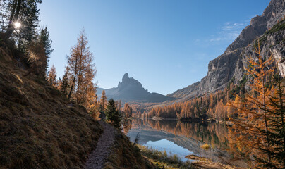 Autumn landscape around lago federa with a hiking path, golden larch trees, and a rocky peak