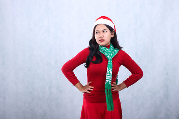 gesture of Asian woman wearing red sweater party wear with Santa hat and scarf, annoyed both hands holding waist and looking to the right, celebrating christmas isolated on white background