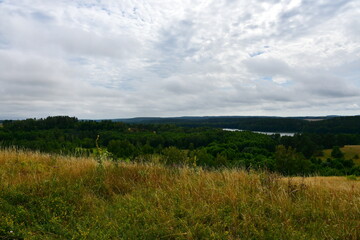 Fototapeta premium A view of a hill or mountain covered from all sides with grass, reeds, forests, and moors, located next to a vast river or lake, meadows, as well as having a view on nearby villages and towns 
