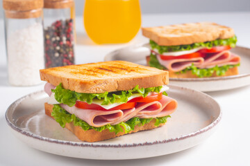 Close-up of two sandwiches with bacon, salami, prosciutto and fresh vegetables on rustic wooden cutting board. Club sandwich concept