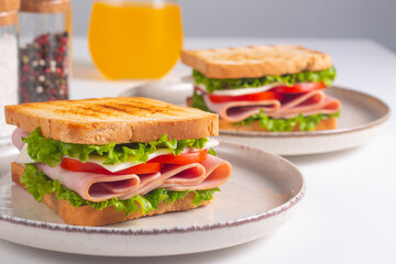 Close-up of two sandwiches with bacon, salami, prosciutto and fresh vegetables on rustic wooden cutting board. Club sandwich concept