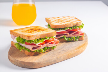 Close-up of two sandwiches with bacon, salami, prosciutto and fresh vegetables on rustic wooden cutting board. Club sandwich concept