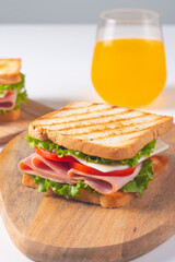 Close-up of two sandwiches with bacon, salami, prosciutto and fresh vegetables on rustic wooden cutting board. Club sandwich concept