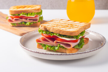 Close-up of two sandwiches with bacon, salami, prosciutto and fresh vegetables on rustic wooden cutting board. Club sandwich concept