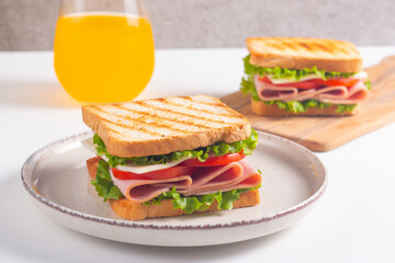 Close-up of two sandwiches with bacon, salami, prosciutto and fresh vegetables on rustic wooden cutting board. Club sandwich concept