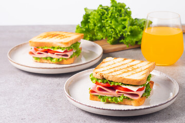 Close-up of two sandwiches with bacon, salami, prosciutto and fresh vegetables on rustic wooden cutting board. Club sandwich concept