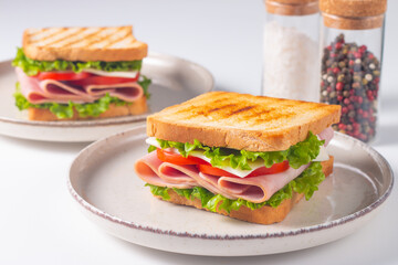 Close-up of two sandwiches with bacon, salami, prosciutto and fresh vegetables on rustic wooden cutting board. Club sandwich concept