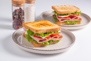 Close-up of two sandwiches with bacon, salami, prosciutto and fresh vegetables on rustic wooden cutting board. Club sandwich concept
