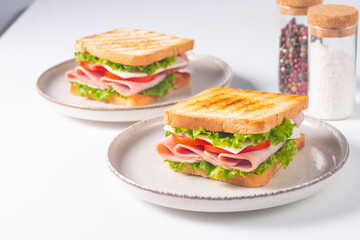 Close-up of two sandwiches with bacon, salami, prosciutto and fresh vegetables on rustic wooden cutting board. Club sandwich concept
