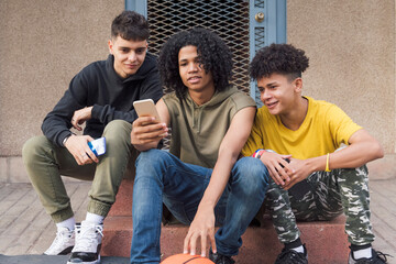 Fototapeta premium three happy multiethnic teen friends sharing mobile phone sitting together with on street, concept of youth and technology of communication