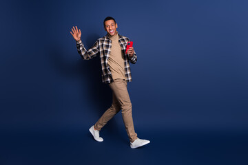 Full length photo of funky cool guy dressed plaid shirt reading modern device waving arm hi emtpy space isolated blue color background