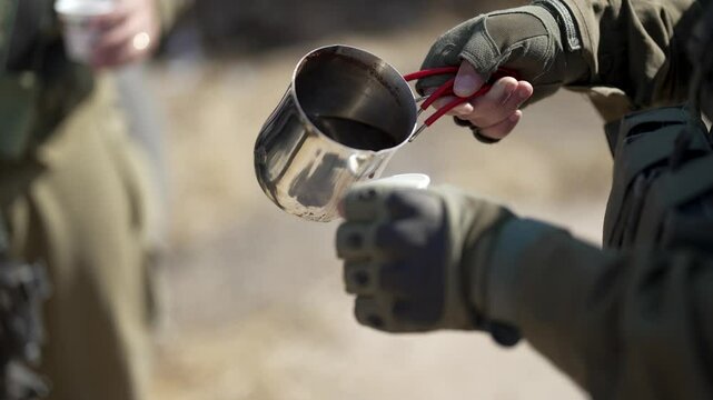 Close-up of a soldier in military uniform pouring coffee into a glass.