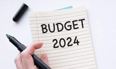 Black marker in hand pointing at open notebook with BUDGET 2024 text on white table