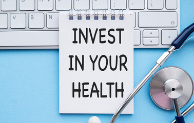 Healthy lifestyle, food and sport concept. Top view of Stethoscope measuring tape pink dumbbell and note book with Invest in your health text on black background.