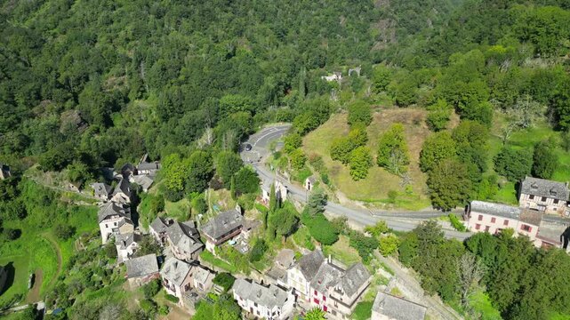 Drone aerial view in France countryside small old medieval town and a cathedral surrounded by a green mountain forest circling around in Conques