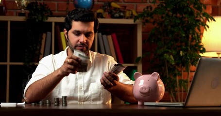 Indian bearded young man managing his finances, counting cash and stacking it into three separate parts for different expenses, symbolizing financial planning and budget management