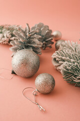 Festive Christmas composition featuring snow-covered branches, glittery pinecones, and shimmering ornaments on a pastel pink background. Perfect for holiday greeting cards