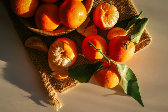 Fresh juicy tangerines with green leaves placed on a rustic burlap cloth, illuminated by warm sunlight. Natural composition perfect for concepts of winter, holidays, and healthy food