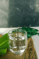 Close-up of a glass of water placed on natural jute fabric with tropical leaves in the background. A minimalist composition showcasing eco-friendly and refreshing aesthetics