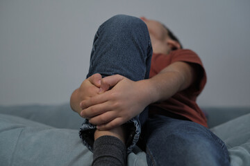 A close-up view of a child sitting with legs folded, hands gently clasped around the knee. The...