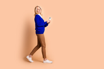 Confident senior woman in stylish attire holding a smartphone, exuding elegance against a beige...