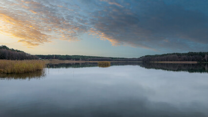 Calm water reflects the tranquil evening sky at a serene lake surrounded by lush forest